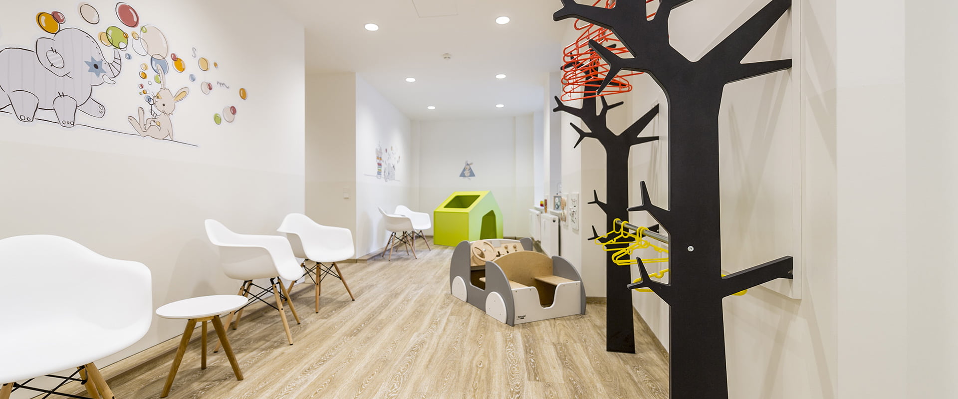 Kinderarztpraxis Hussack Leipzig Wartezimmer mit kinderfreundlichen Wandbildern, einer Garderobe in Form von Bäumen und einem Spielzeug-Auto