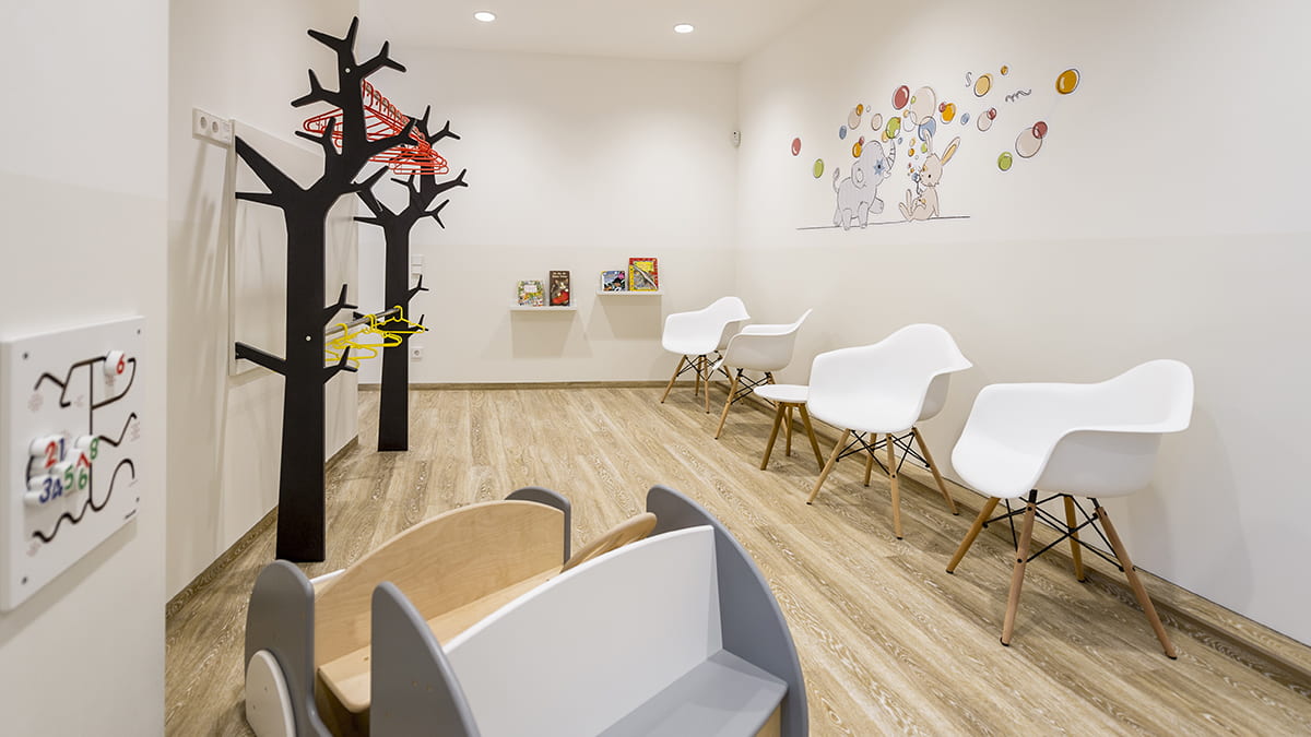 Kinderarztpraxis Hussack Leipzig Blick vom Wartebereich in Richtung Empfangsbereich mit Wandregalen, Bildern, der Garderobe und Stühlen im skandinavischen Design