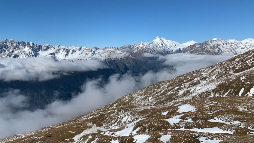 Blick auf mit Schnee bedeckte Berge unter blauem Himmel und Nebel in Richtung Tal
