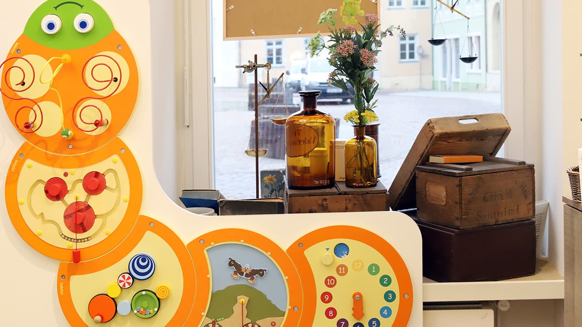 Löwen-Apotheke Oschatz Detailaufnahme Schaufenster und bunte Raupe mit verschiedenen Spielen für Kinder an der Wand