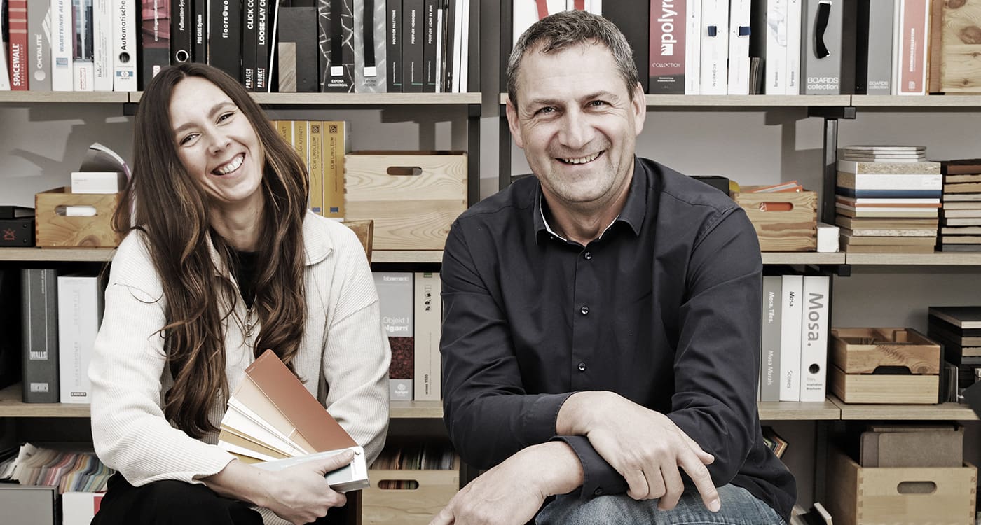mediraum design Teamfoto Hagen Brockhaus & Elisa Borchert sitzen in die Kamera lächelnd vor einem Regal mit vielen Büchern & Holzkisten