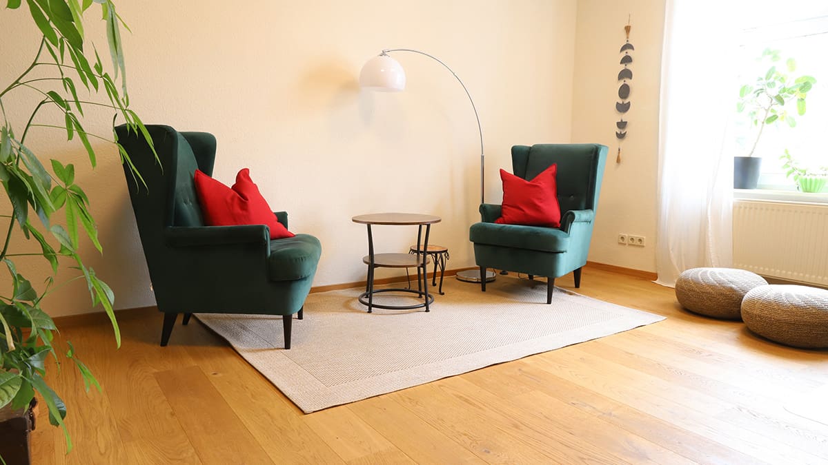 Referenz Praxis für Psychotherapie Peterhänsel Leipzig Sprechzimmer in gemütlicher Atmosphäre mit zwei grünen Sesseln, einem kleinen Tisch und einer weißen Stehlampe auf einem Teppich