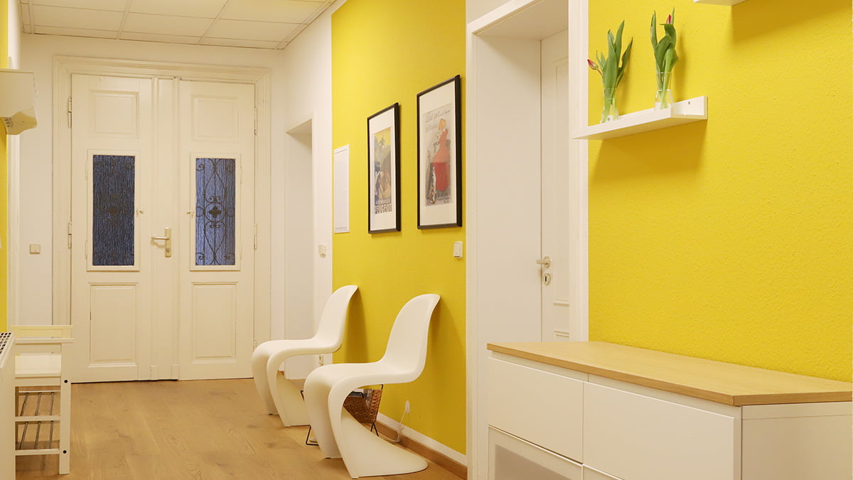Referenz Praxis für Psychotherapie Peterhänsel Leipzig Eingangsbereich mit gelber Wandfarbe, Möbeln in weißer Farbe und Bildern sowie Blumen